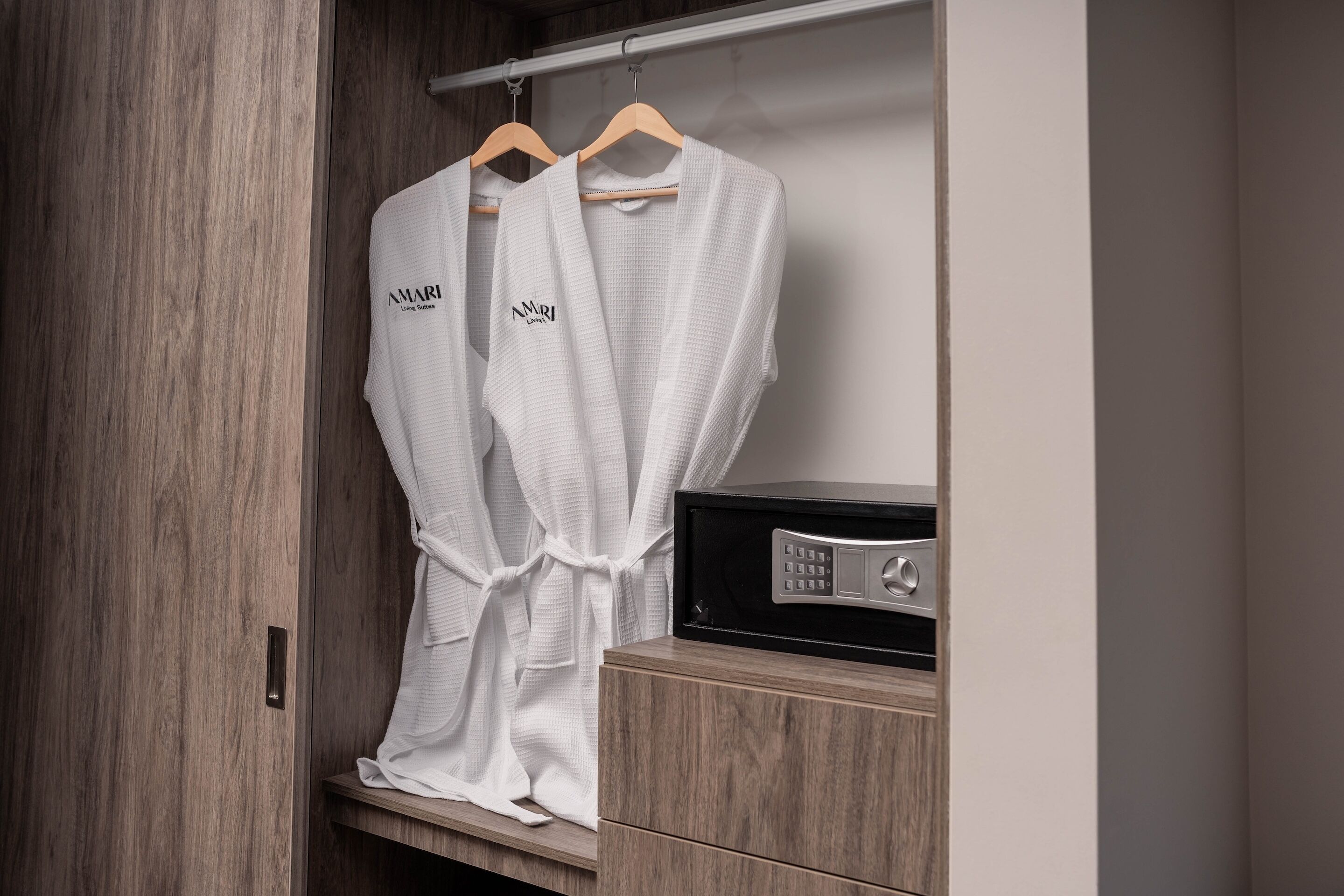 A wooden wardrobe with two white robes hanging on a wooden hanger.