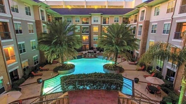 Un hôtel à plusieurs étages doté d’une cour intérieure comprenant une piscine, des palmiers, des espaces de détente en plein air et un escalier menant aux étages supérieurs.