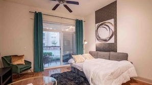 Une chambre à coucher avec un lit, un fauteuil vert, une table en verre et un balcon avec des rideaux.