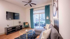 Un salon moderne doté d’un téléviseur à écran plat, d’un ventilateur de plafond, d’un canapé, d’une table basse et offrant une vue sur l’extérieur grâce à de grandes fenêtres.
