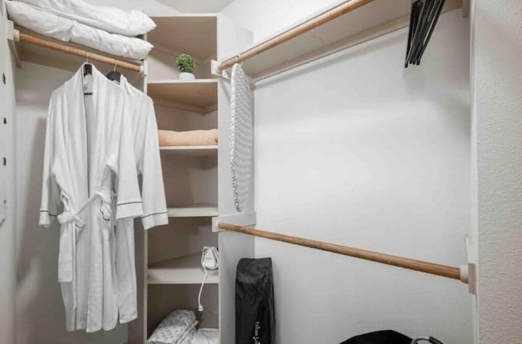 Un armario ordenado con batas blancas, estantes y una barra de madera.