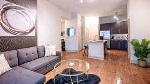 Un salon moderne avec un canapé, une table basse en verre et une cuisine en arrière-plan.
