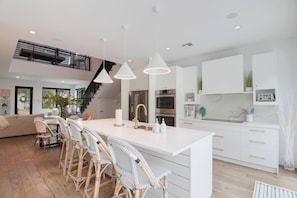 Una cocina moderna con armarios blancos, una isla central y un comedor con sillas de mimbre.
