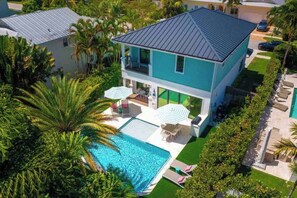 Una casa moderna de dos pisos con piscina, rodeada de exuberante vegetación y palmeras.