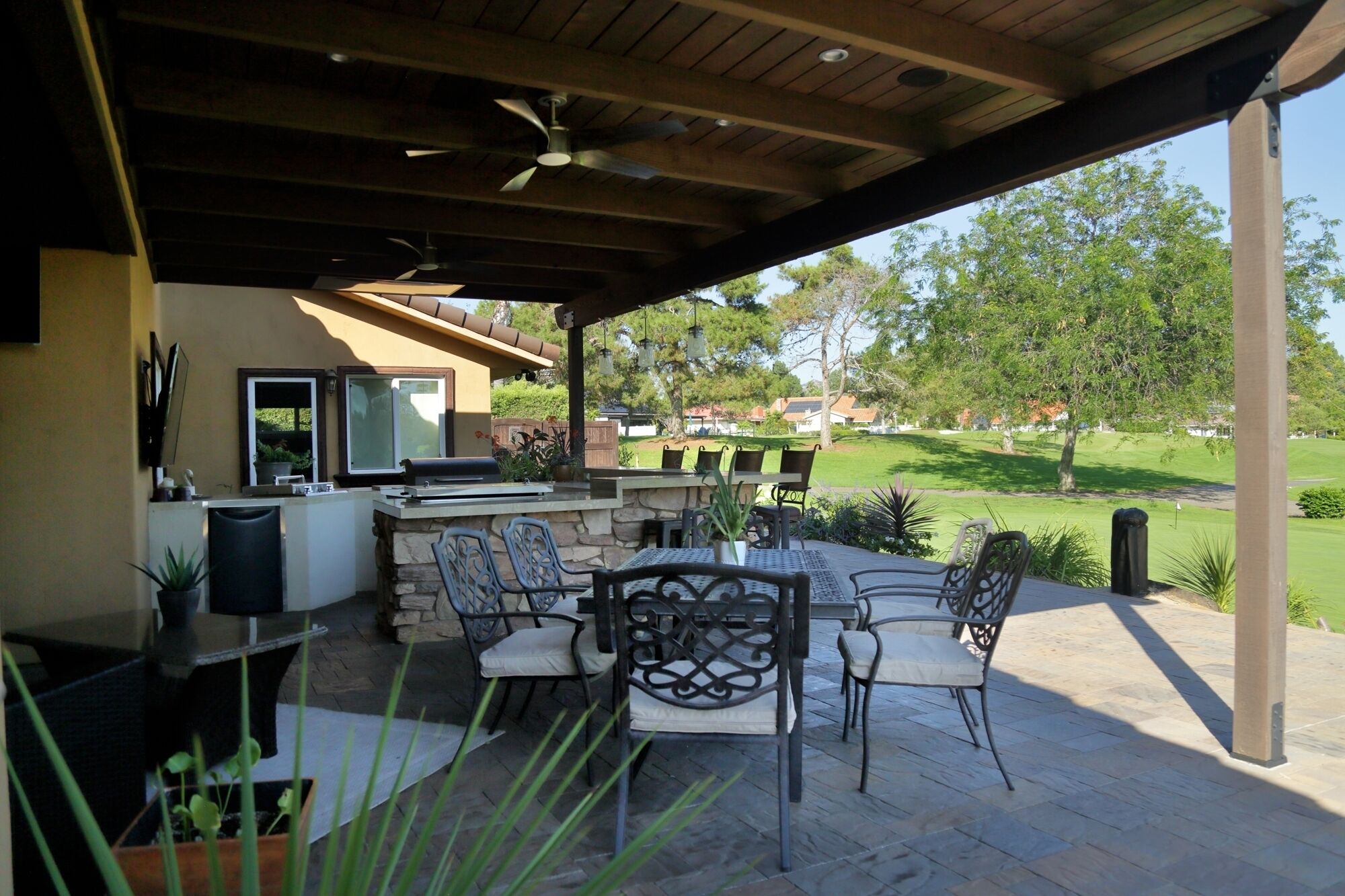 An outdoor patio with a stone barbecue, outdoor seating, and a view of a golf course.