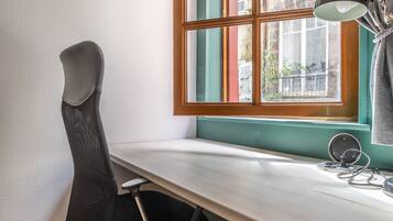 Een modern bureau met een zwarte bureaustoel, een raam met uitzicht op gebouwen, en een bureaulamp.