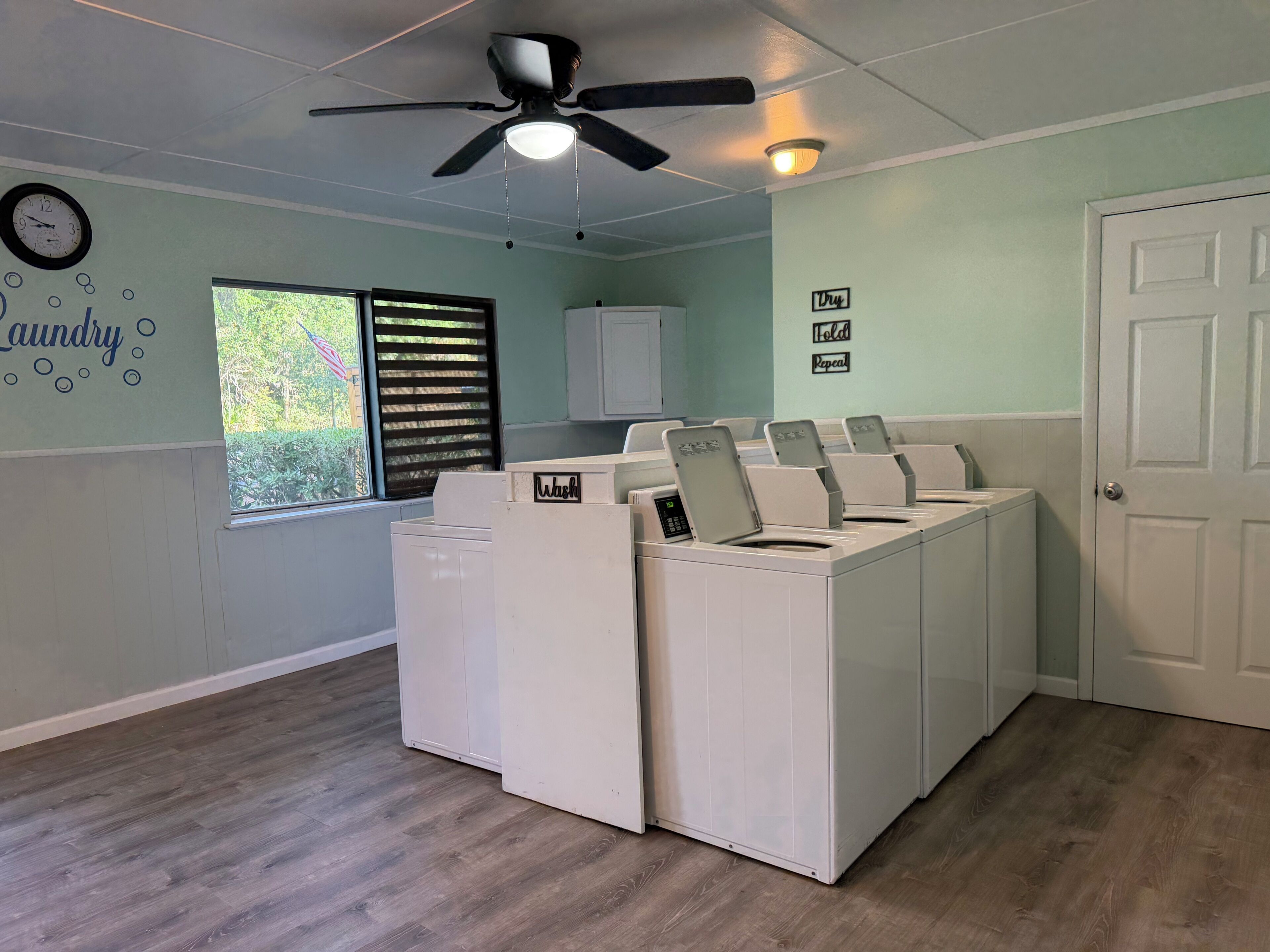 A laundry room with a ceiling fan, a clock, and a window with blinds.