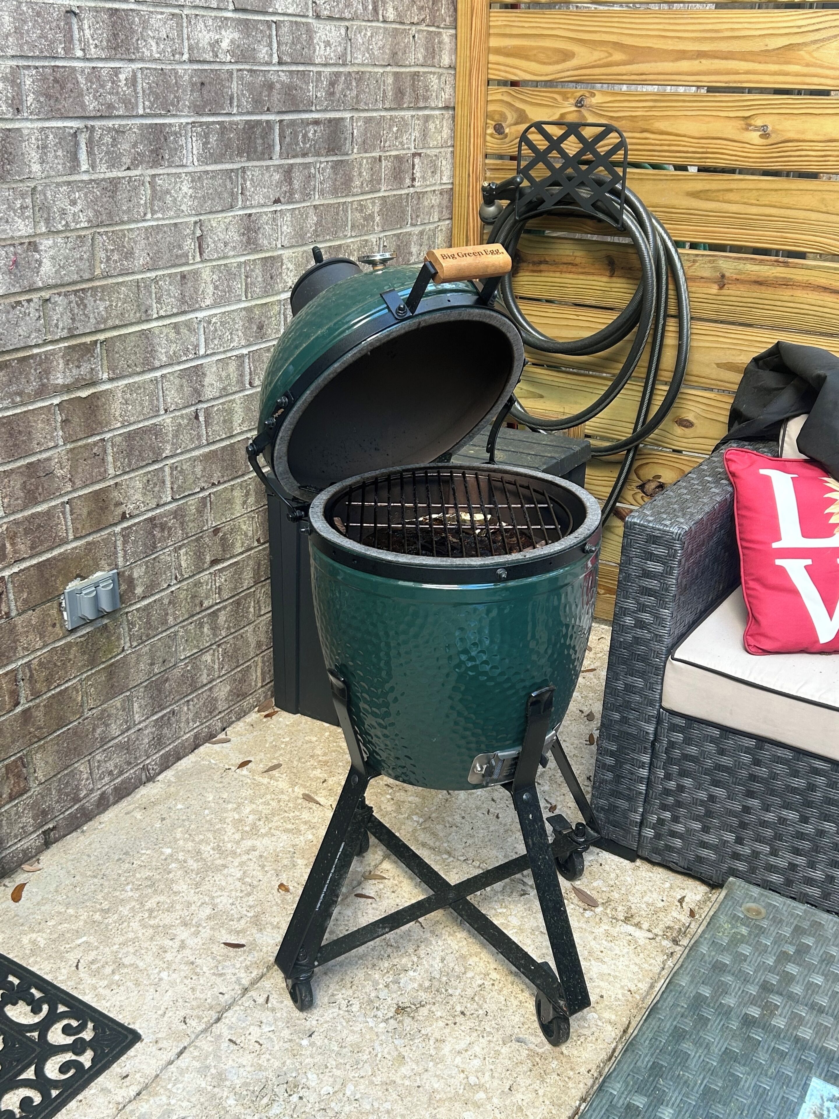 A portable grill with a lid open, placed on a stand in an outdoor setting.