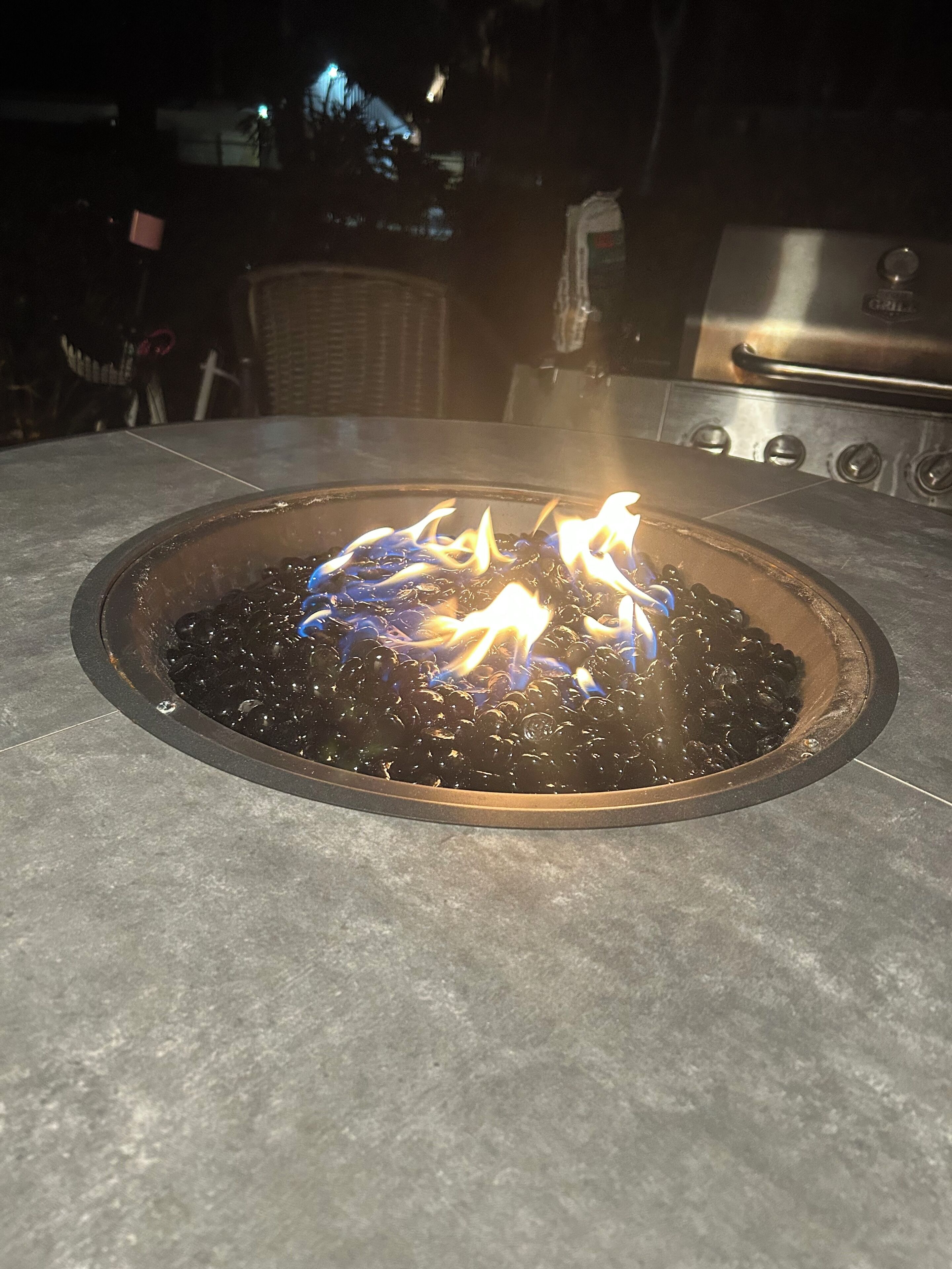 A fire pit with flames, surrounded by a stone patio.