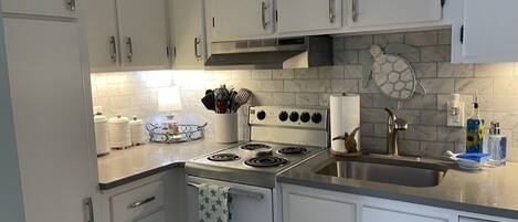 Una cocina con armarios blancos, estufa, fregadero y salpicadero de azulejos.