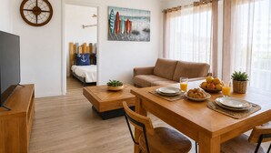 Un soggiorno moderno con zona pranzo, un letto vista, una sveglia e un quadro con tavole da surf.