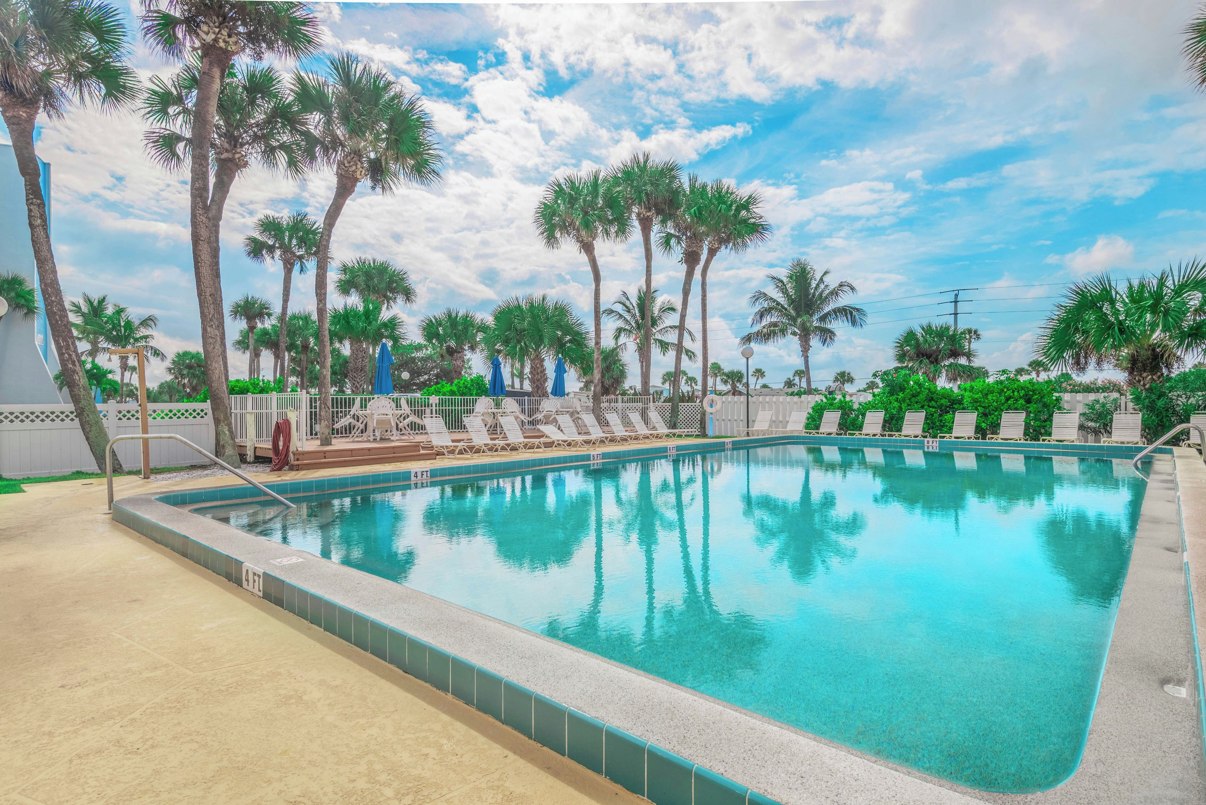 A swimming pool with clear blue water, surrounded by palm trees and lounge chairs.
