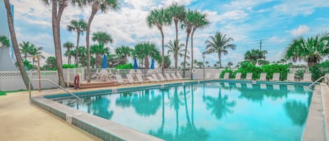Une piscine à l’eau d’un bleu cristallin, entourée de palmiers et de chaises longues.