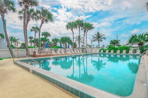 Une piscine à l’eau d’un bleu cristallin, entourée de palmiers et de chaises longues.