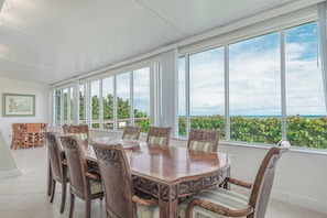A dining area with a large table and chairs, large windows with a view of the ocean and greenery. - Getaways at Turtle Reef Club (Jensen Beach)