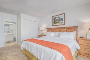 A bedroom with a bed, a wooden headboard, a nightstand, a lamp, a framed picture on the wall, and a closet with sliding doors.