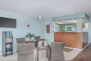 A reception area with a counter, a television mounted on the wall, and a seating area with chairs and a table. - Getaways at Turtle Reef Club (Jensen Beach)