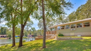 A lakeside house with a deck, a stone retaining wall, and a grassy lawn. - Kilgore Lakefront Home w/ Private Dock & Pier! (Kilgore)