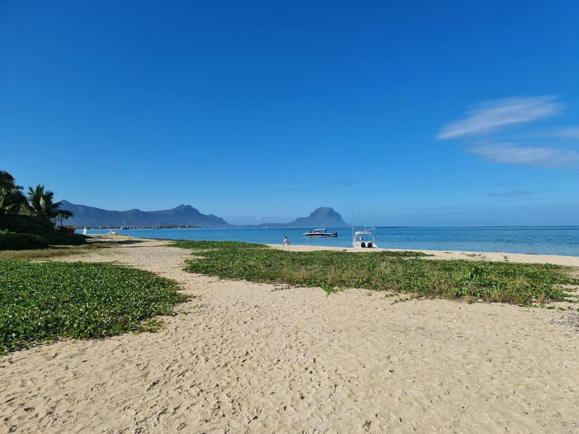 A beach with a clear sky, a sandy path, and boats in the water.