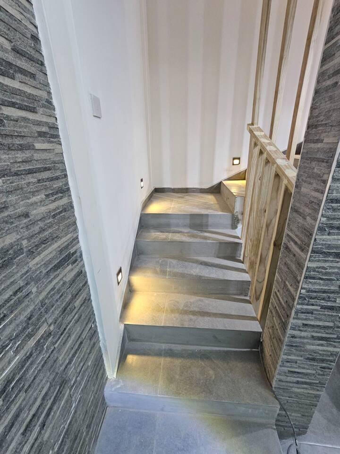 A staircase with a stone wall on one side and a wooden railing on the other.