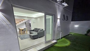 Un interior moderno con un sofá gris, una zona de comedor y una escalera que sube a un nivel superior.
