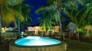 Uma piscina circular rodeada por palmeiras e um edifício com telhado vermelho.