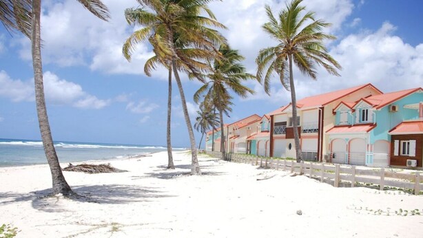 Um hotel à beira-mar com vários edifícios coloridos, palmeiras e uma praia de areia.