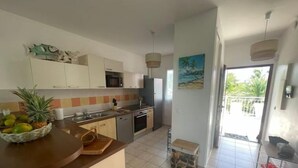 Cozinha moderna com armários brancos, micro-ondas e pia. Há uma fruteira no balcão e uma pequena mesa com uma cadeira.