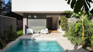A modern outdoor pool area with a clear view of the pool, two white lounge chairs, and a wooden deck. - Athenian Riviera Prime Residence  (Vari-Voula-Vouliagmeni)
