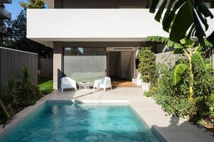 Uma área moderna de piscina ao ar livre, com vista clara para a piscina, duas espreguiçadeiras brancas e um deck de madeira.