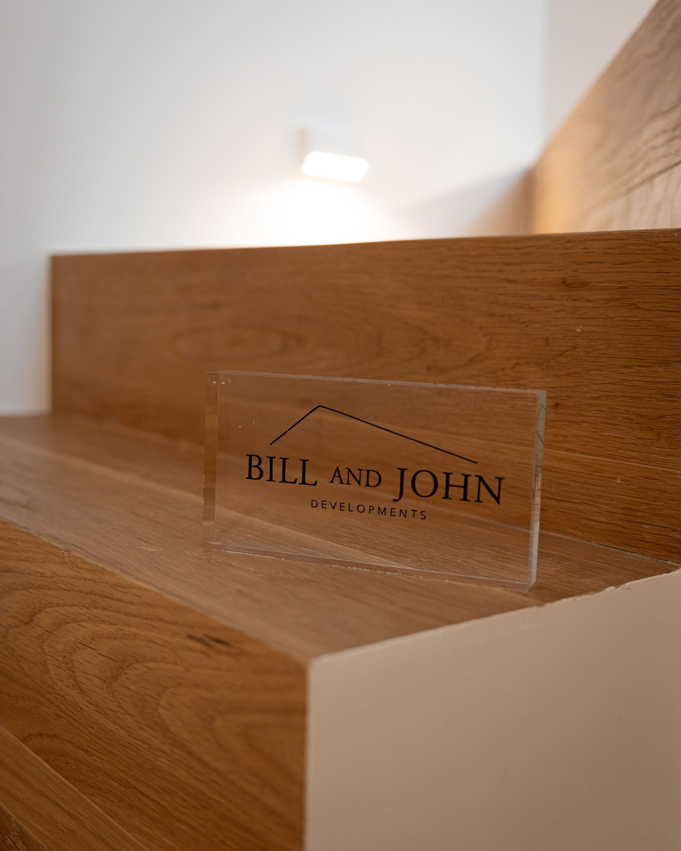 A clear acrylic sign with the text "BILL AND JOHN DEVELOPMENTS" on a wooden surface.