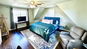 Ein Schlafzimmer mit Bett, Deckenventilator, Fernseher, Schreibtisch, Stuhl und Fenster.
