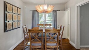 Ein Esszimmer mit Holztisch und Stühlen, einem modernen Kronleuchter und einem großen Fenster mit Vorhängen.