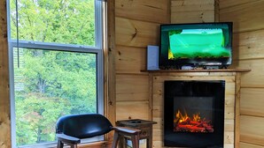 A cozy cabin interior with a wooden chair, a fireplace, and a television mounted above it. - ONYX OWL CABIN: Private Hot Tub⁘Fire Pit⁘Heated Patio⁘Vineyard⁘Hiking⁘Golf (Scaly Mountain)