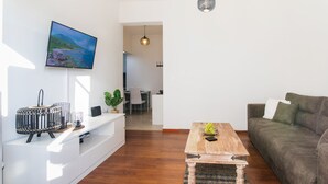 A modern living room with a flat-screen TV, a wooden coffee table, a sofa, and a dining area in the background. - Midtown Apartment by CorfuEscapes (Corfu)