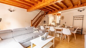 Una sala moderna con techo de madera, un sofá modular gris, una mesa de centro blanca y un comedor con sillas blancas y una mesa de madera.