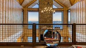 A spacious room with a high ceiling, wooden walls, and large windows offering a view of the landscape. - Moonshiners Hideout | Swing Bed, Hot Tub & Mountain Views (Gatlinburg)