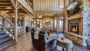 A spacious living room with a fireplace, a leather sofa, and a staircase leading to an upper level. - Moonshiners Hideout | Swing Bed, Hot Tub & Mountain Views (Gatlinburg)