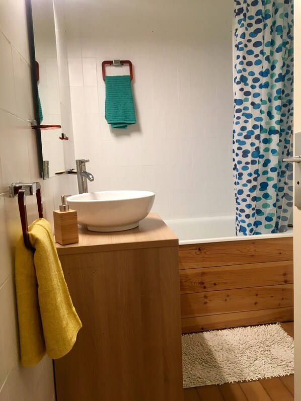 A bathroom with a white sink, wooden vanity, a mirror, a towel rack, a shower curtain, and a white fluffy rug.