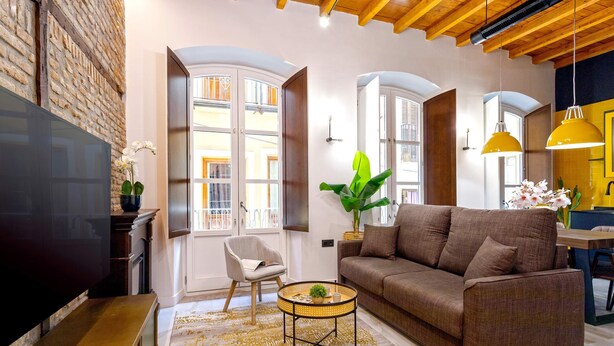 A living room with a brown sofa, a round coffee table, and a TV. There is a chair and a plant on the floor. - Genteel Home Catedral 101 (Granada)