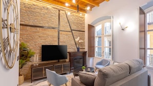 A cozy living room with a stone wall, a fireplace, a flat-screen TV, and comfortable seating. - Genteel Home Catedral 201 (Granada)