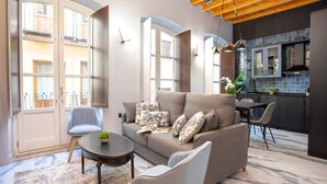A modern living room with a sofa, chairs, a coffee table, and a kitchen area with cabinets and a dining table. - Genteel Home Catedral 201 (Granada)