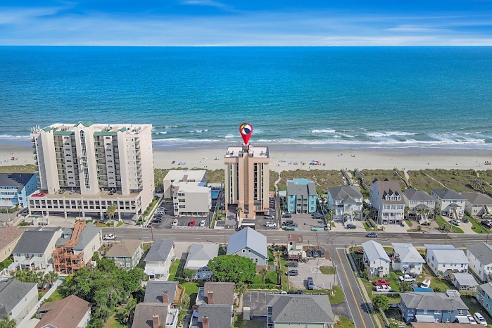 Ein Küstenwohngebiet mit einem markanten Hotel und Blick auf den Strand, mehrstöckigen Gebäuden und blauem Himmel.