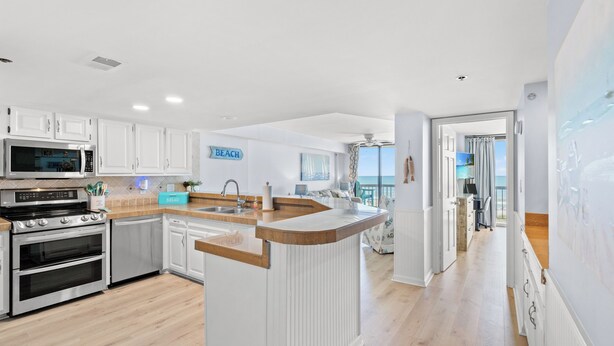 A modern kitchen with white cabinetry, a central island, and a view to the living area.