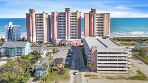 Un complejo hotelero costero con varios edificios altos, un estacionamiento y vista al océano.