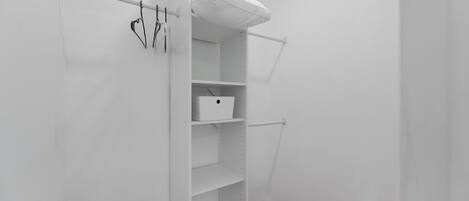 A white closet with shelves and hanging space, a white box on one shelf, and a white towel on a shelf.