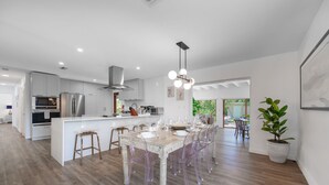 A modern kitchen with stainless steel appliances, a central island with bar stools, and a dining area with a wooden table and chairs. - Home in Westchester Miami - Private Pool (Miami)
