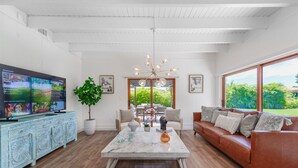 A spacious living room with a large flat-screen TV, a coffee table, a sofa, and a dining area with a view of greenery outside. - Home in Westchester Miami - Private Pool (Miami)