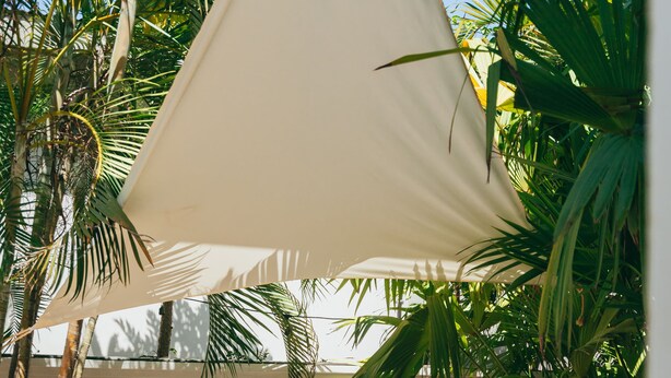 A cozy outdoor seating area with a cushioned bench, a woven stool, and a large canopy providing shade. - Dream Surf House Avellana (Tamarindo)