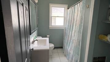 A bathroom with a white sink, toilet, and a window with a shower curtain.